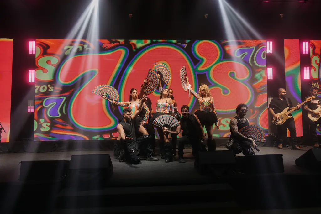 Grupo em pose no momento anos 70, feixes brancos cruzando o palco