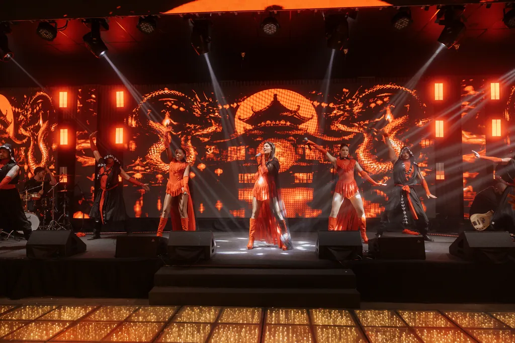 Vista geral do palco com o cenário oriental e o grupo em coreografia