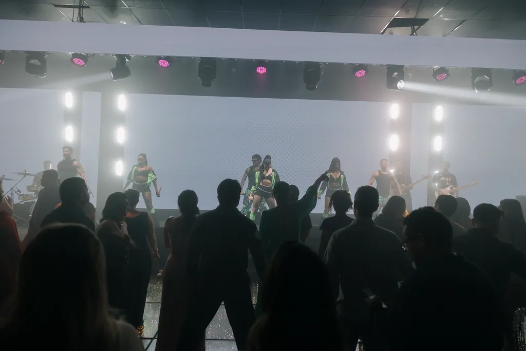 Público em silhueta diante do palco iluminado de branco